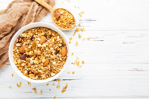 Tasty granola in bowl and spoon on white wooden background