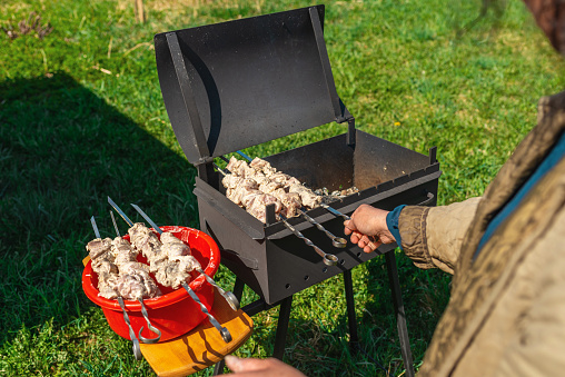 Woman strands raw pieces of marinatedo pork meat on long skewers frying shish on the grill.Nice summer day.