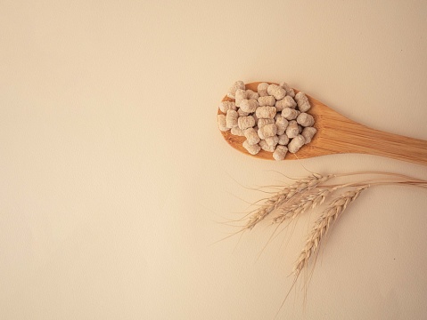Extruded bran on a wooden spoon and wheat spikelets on a beige background with a place to copy. The concept of proper snacking, proper nutrition and weight loss.