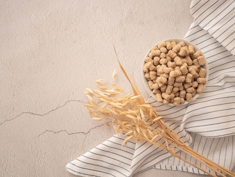 Extruded bran in a white plate with a striped towel and oat spikelets on a light plaster background. The concept of proper snacking, proper nutrition and weight loss.
