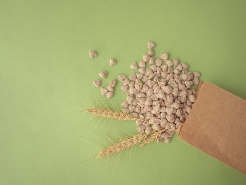 Extruded bran in the shape of a heart is poured out of the package onto a green background. Spikelets of wheat. The layout for the label. A place for the text.