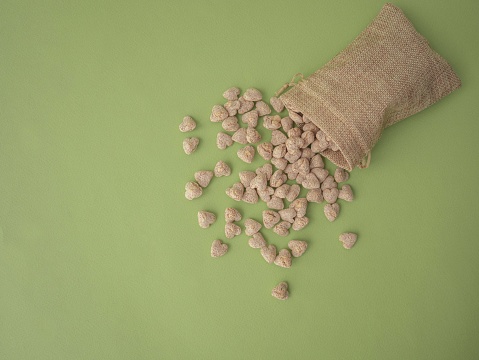 Extruded bran in the shape of a heart is poured out of a cloth bag onto a green background with space for text.