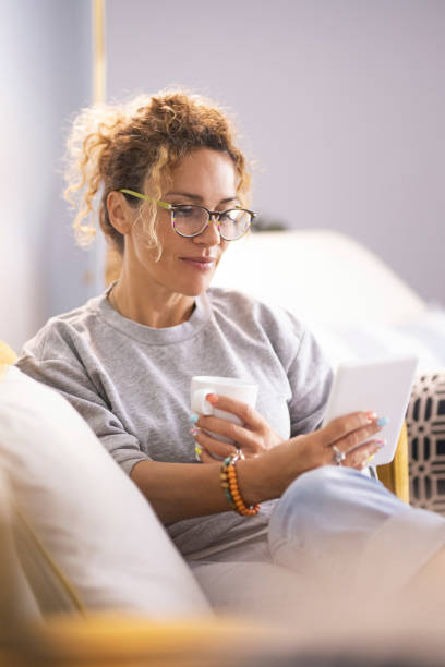 istock Modern lady having relax at home sitting on couch and using ereader tablet to read an online ebook. Woman using technology indoor leisure activity alone enjoying relaxation on couch. Indoor life 2068148307