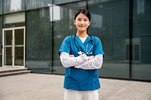 Happy nurse in blue standing outside with arms folded