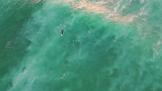 Aerial view surfer swimming in ocean summer weekend. Top shot unrecognizable surfboarder lying on board waiting perfect wave. Beautiful turquoise sea water rocking unknown person in super slow motion.