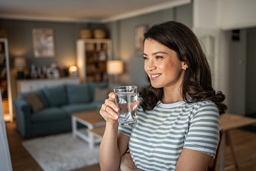 Smiling young beautiful woman drinking a glass of fresh clean water