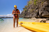 A woman stands in shallow sea water and prepares to paddle a kayak in the open sea