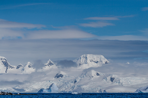 A tranquil Antarctic landscape, near Mikkelsen Harbour on Trinity Island, highlighting stark reflections, rugged mountains, and impressive icebergs