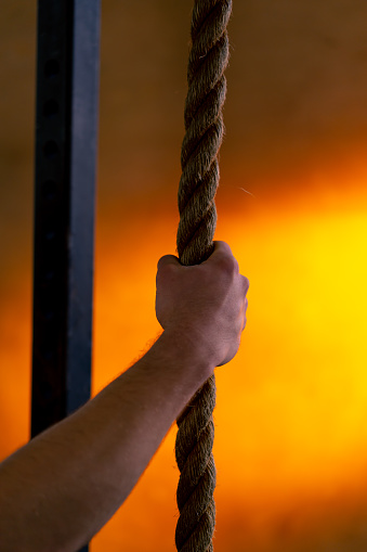 close-up in a sports club of a hand holding ropes for exercise on a bright orange background