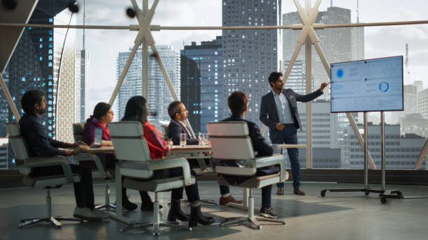 istock Diverse Indian Office Conference Room: Young South Asian CEO Makes a Presentation for Entrepreneurs, Talking, Using TV with Infographics and Statistics. Businesspeople Talk About an Ecommerce Startup 2068223900