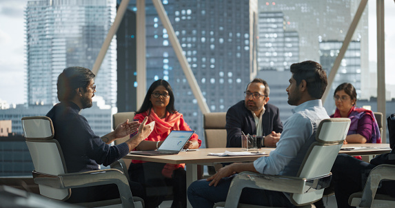 Finance Department Having a Meeting to Discuss a Project with a Team Leader. South Asian Colleague Using Laptop Computer, Working in Modern Office, Employees Having a Conversation in a Conference Room