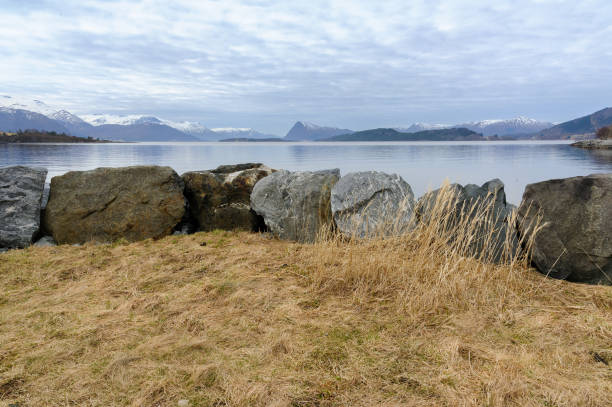 Tranquil scene showing the calm sea, boulders, and mountains under a soft evening sky.