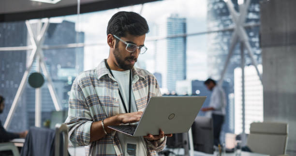 istock Indian Male Business Analyst Standing with Laptop Computer in a Modern Office. Successful Man Assessing Technological Risks And Developing Strategies For Company Growth and Expansion 2068231741
