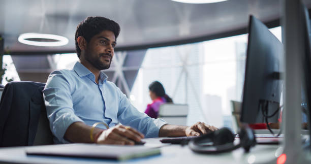 istock Portrait of a South Asian Financial Securities Trader Working on Desktop Computer in a Modern Office. Handsome Indian Accountant Bookkeeping Financial Affairs of a Business Venture 2068233323