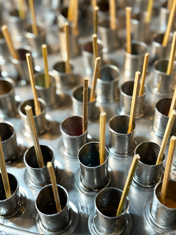 Stock photo showing close-up, elevated view of a stainless steel lid to a street food stall lollypop maker. A stainless steel drum container has been filled with ice cubes, salt and water before a lid with holes for metal tube moulds was added. Flavoured juice is the poured into each tube and a bamboo stick added. The tubes are then agitated by turning the lid via it's handles to encourage the lollypops to freeze quicker.
