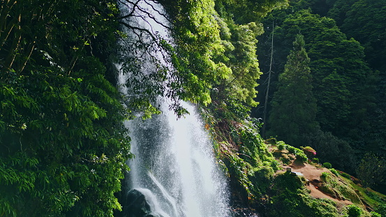 Woodland waterfall falling rocks closeup. Drone shot vivid water cascading mossy wild rainforest. Big raging stream rushing down stones among lush forest greenery. Relaxing nature landscape concept.