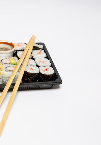 Sushi to go in a black takeaway box with wooden chopsticks isolated on white background with copy space