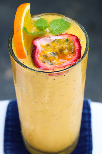 Stock photo showing close-up, elevated view of drinking glass filled containing mango, orange and passionfruit juice smoothie as part of a healthy breakfast.