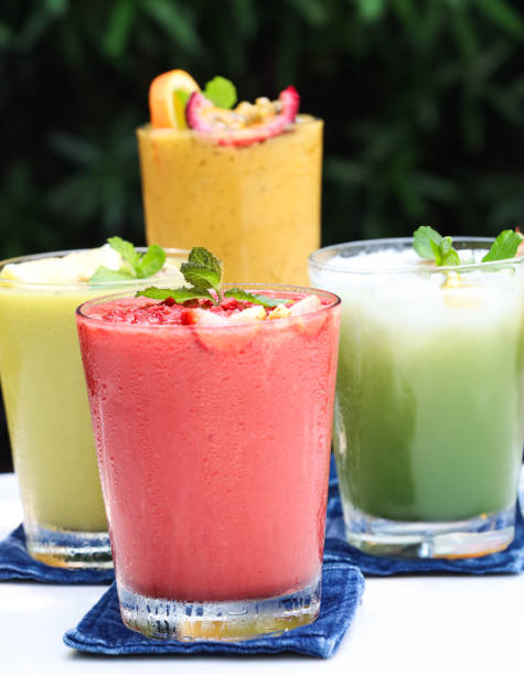 Stock photo showing close-up view of four drinking glasses filled with ice cubes and containing iced matcha latte, strawberry, orange and passionfruit juice, and avocado, spinach and kiwi juice smoothies as part of a healthy breakfast.