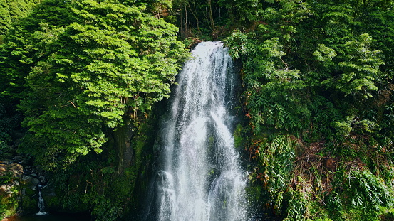 Powerful waterfall falling tropical forest. Drone shot of raging water flowing stones cascade splashing rocks in summer day. Beautiful vivid stream in green jungles. Picturesque nature landscape.