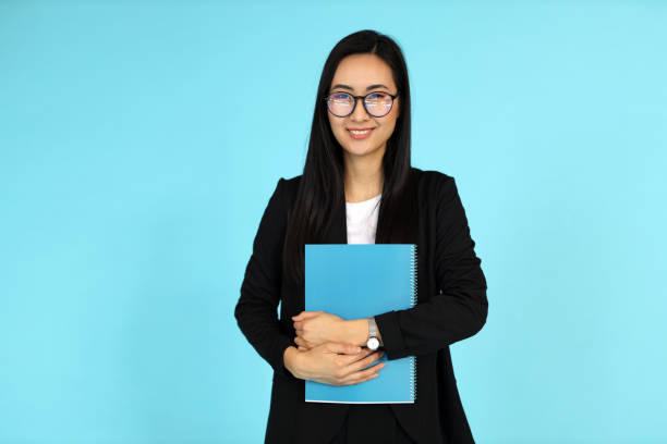 istock An Asian woman, against a blue background, holds documents, embodying confidence and academic success. 2068292287