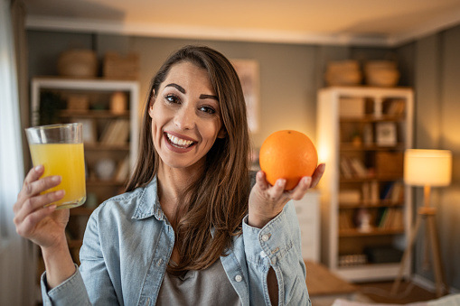 A young woman exudes cheerfulness as she enjoys the moment of drinking fresh orange juice. Her beauty stands out and the smile on her face reflects the joy and pleasure she feels as she drinks the refreshing drink.