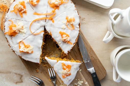 Carrot cake with white sugar icing on a wooden cutting board with knife and cake forks from above