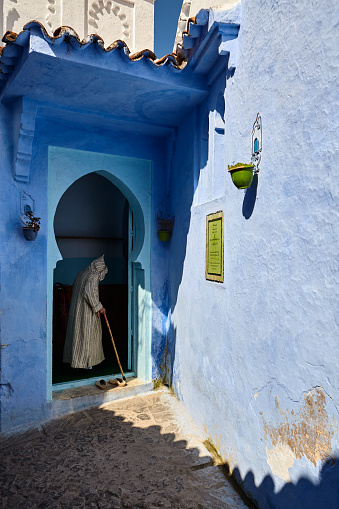 Blue city street with Moroccan man in traditional white djellaba entering mosque in Chefchaouen, Morocco, North Africa.