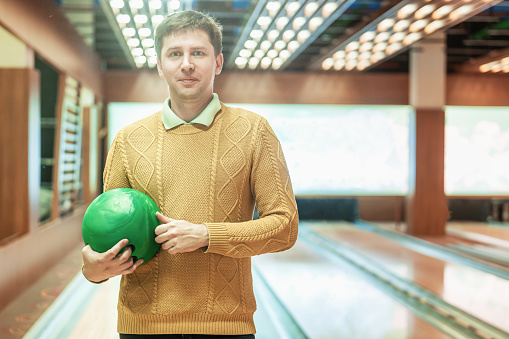 Smiling man in holding green bowling ball at bowling alley.
