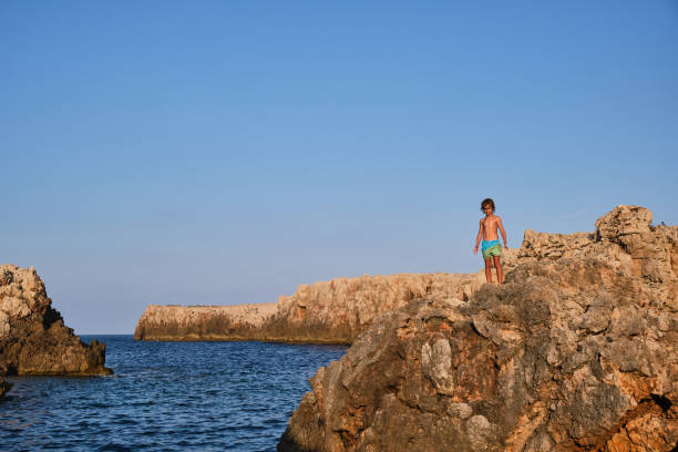 istock Boy standing on rock near blue sea 2068386621