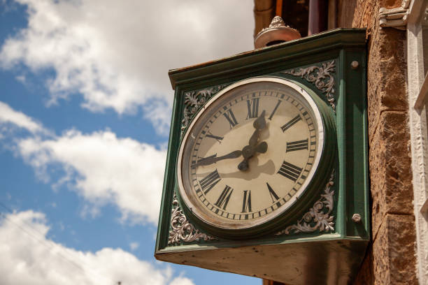 istock An ornate vintage clock mounted on a brick wall, displaying time under a clear blue sky with wispy clouds 2068387165
