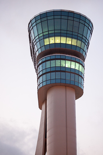 An illuminated modern airport control tower stands tall against the dusky sky, highlighting aviation progress.