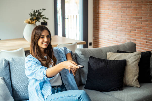 istock young woman sitting on her home sofa, holding the TV remote while enjoying a program. she is enjoying her leisure time at home. One female people using control tv watching movie alone on the couch 2068397810