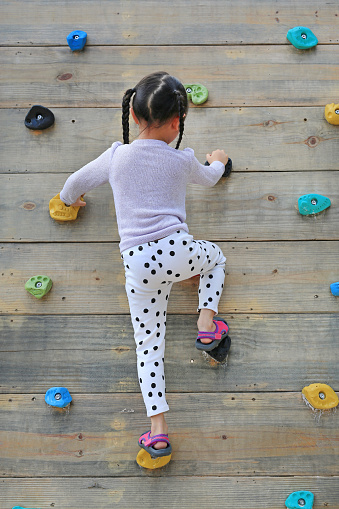 Little child girl trying on free climbing on the playground wooden wall outdoors.