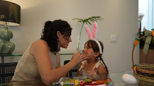 Mother painting daughter face during the easter holiday at home