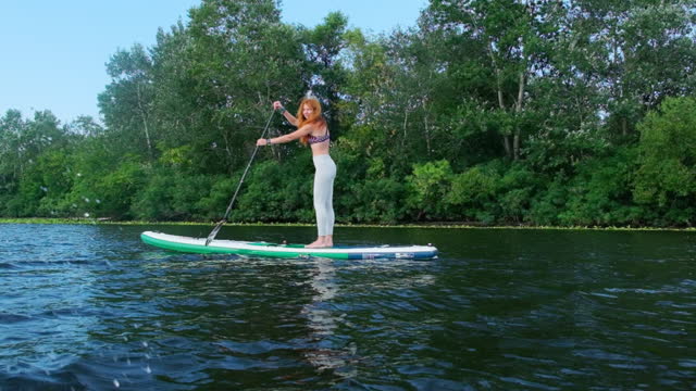 Woman maneuvers on SUP board on water utilizing paddle