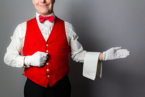 Smiling Waiter or Butler in Red Vest With Welcoming Gesture