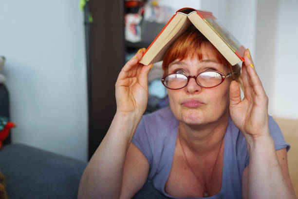 Red-haired woman with glasses emotionally reads book, expression emotions and passion on face, in home interior