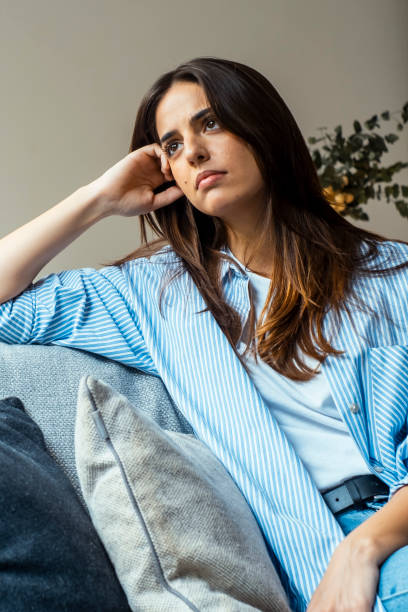 istock Thoughtful young woman with sad expression sitting on sofa at home looking outside and thinking bad problems on life. Lonely depressed adult female. Negative pessimistic emotions people portrait life 2068434369