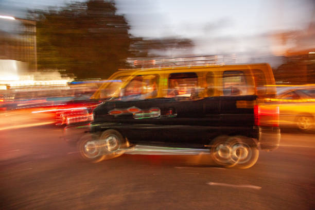 A blurry image of a black van with a yellow roof. The van is driving down a street at night