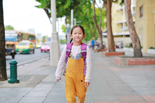 Happy Asian child girl walking with student shoulder schoolbag. Little schoolgirl with a backpack front view. Back to school concept.