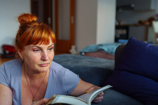 Red-haired woman with glasses emotionally reads book, expression emotions and passion on face, in home interior