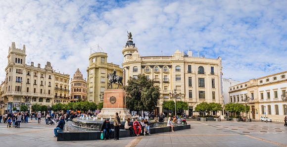 People sitting on the edge of the fountain where stands the equestrian monument to Gonzalo Fernández de Córdoba, work by Mateo Inurria in 1923. The location is the Plaza de las Tendillas, one of the popular squares in the Cordoba downtown (4 shots stitched)
