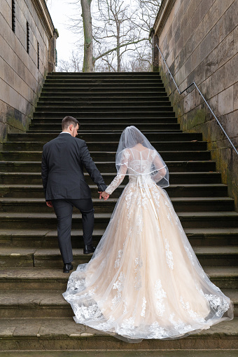 The bride and groom are walking along the stone steps of an ancient building, a palace. Rear view, from the back. The bride is wearing a beautiful long dress.