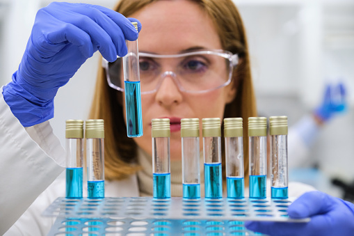 Professional female researcher examining blue test tubes. Scientific research.