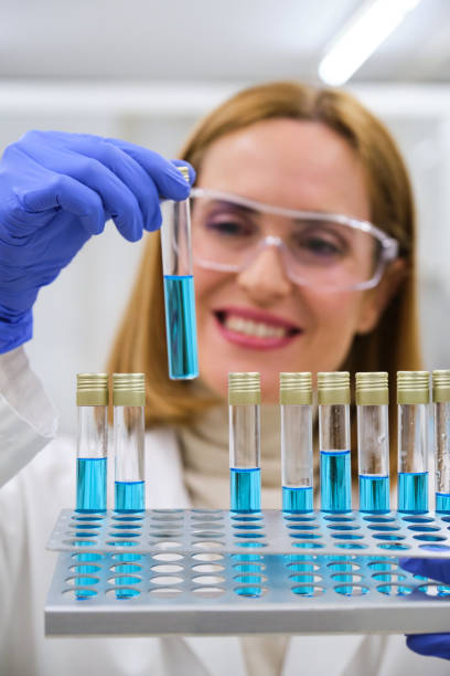 professional female researcher smiling and examining blue test tubes. - test cricket zdjęcia i obrazy z banku zdjęć