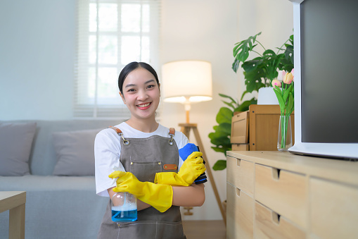 A woman in a cleaning outfit is smiling and holding a bottle of cleaner and a mop. Concept of cleanliness and orderliness