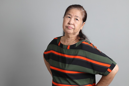 The 70s Chinese senior woman with casual clothes standing on the grey background.