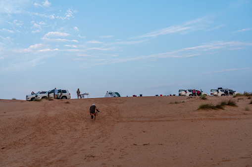 Small group of tourists camping in Wahiba desert with tent and cars in Oman.