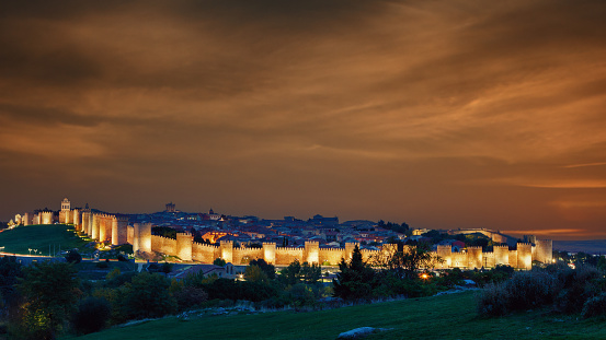 Panoramic view of the city of Avila, Spain, with its famous illuminated medieval walls surrounding the city at dusk